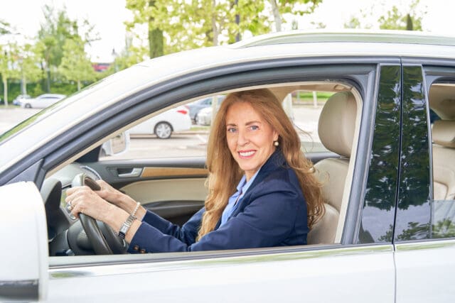 portrait of a woman in her 50's driving a car, side view of a female driver looking at the camera